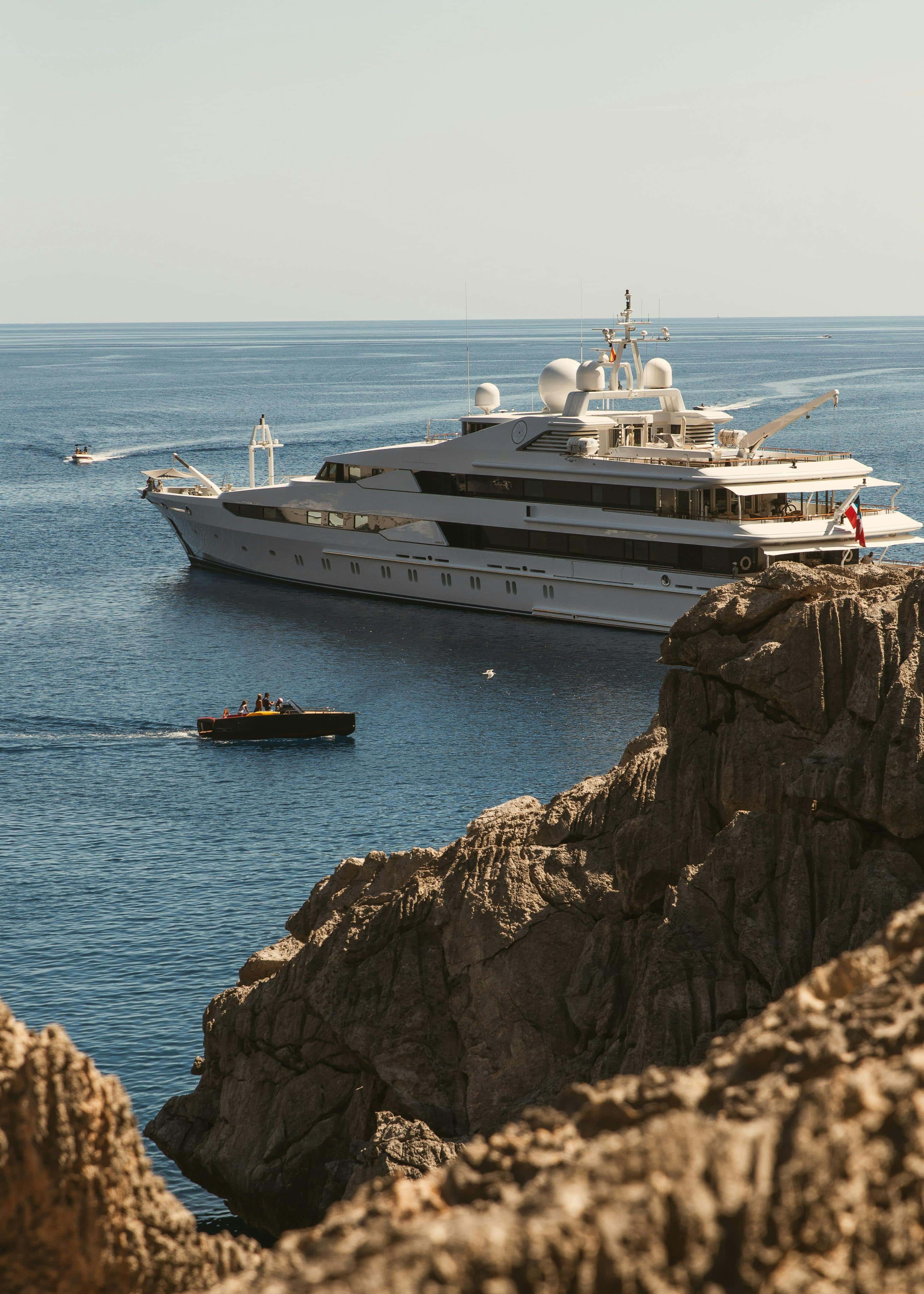 Superyacht anchored off rocky coastline